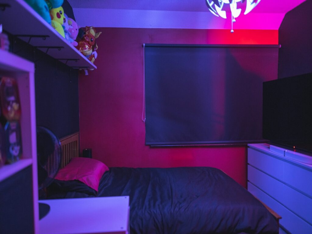 Modern bedroom with color-changing LED strip lights behind the headboard and along shelves, illustrating types of mood lighting for a customisable glow.